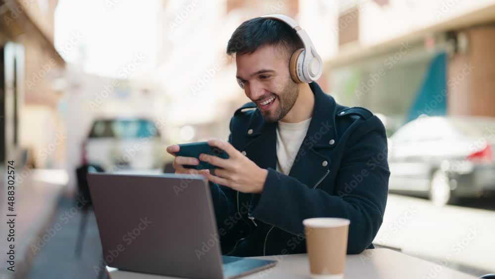 Young hispanic man playing video game sitting on table at coffee shop terrace Young hispanic man playing video game sitting on table at coffee shop terrace