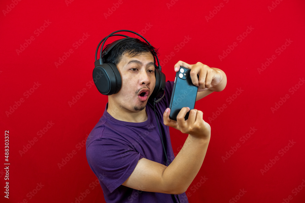 An asian man is playing a game on his smartphone and wearing a headset. An asian man is playing a game on his smartphone and wearing a headset.