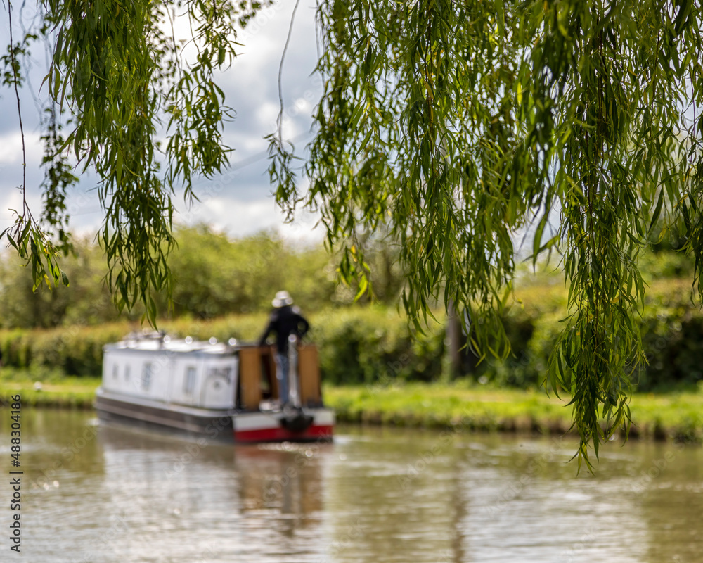 Defocused narrowboat on a canal seen through the leaves of a weeping willow