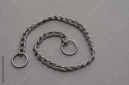 Silver metal chain with two rings on a gray background. Tugging dog leash.