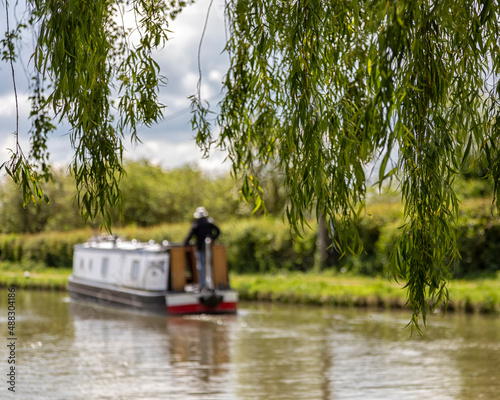 Fotografia Defocused narrowboat on a canal seen through the leaves of a weeping willow