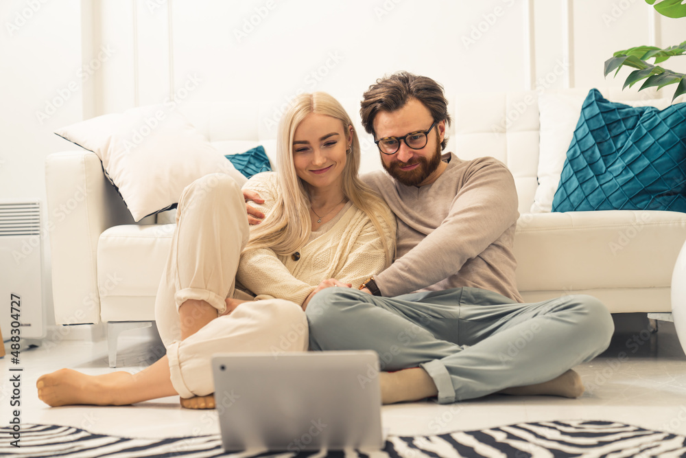 caucasian blonde long-haired beauty sitting on the floor with her affectionate partner and watching videos on their laptop. High quality photo