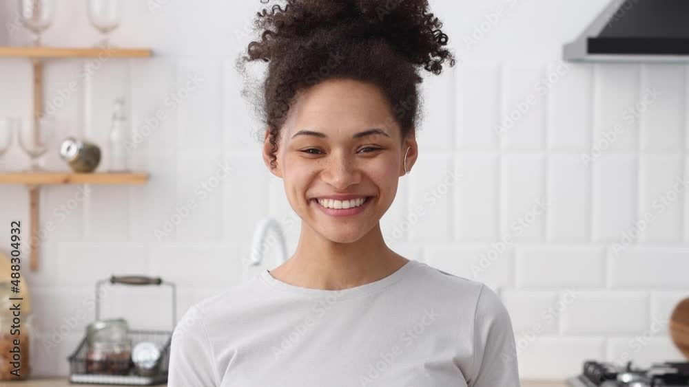 Close up head shot beautiful African young woman standing alone in home kitchen looking at camera and smiling friendly, having wide toothy charming smile Close up head shot beautiful African young woman standing alone in home kitchen looking at camera and smiling friendly, having wide toothy charming smile