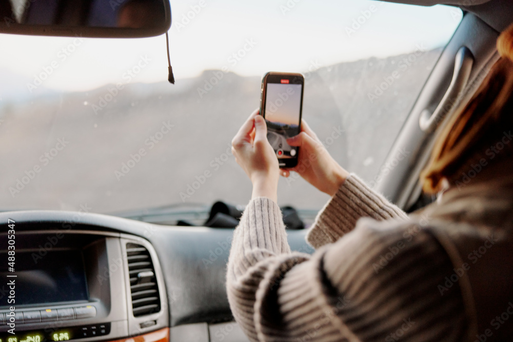 Naklejka premium woman in a car takes pictures of nature on the phone