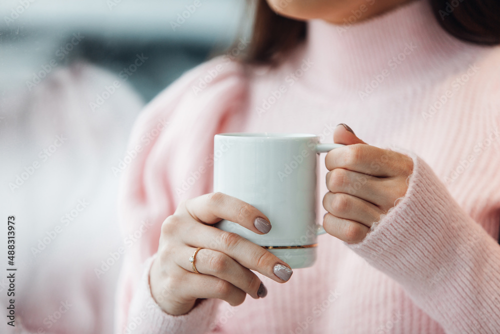 The woman is holding a mug with coffee inside of the modern apartment The woman is holding a mug with coffee inside of the modern apartment