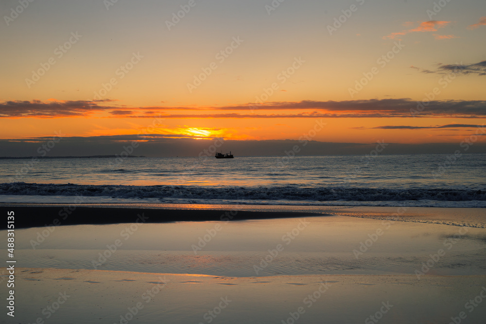 Sunrise over the sea with sky reflection on the shore and a ship on the horizon