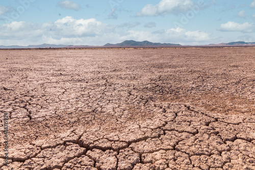 A cloudy bright sky over a barren dry desert mud crack landscape with mountains in the background
