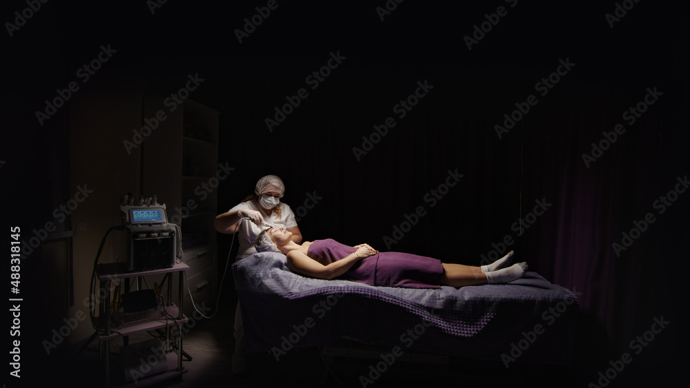 Naklejka premium Woman cleansing facial in spa salon. Water oxygen face h2o2 small bubble facial rf lifting equipment skin care microdermabrasion machine. Wellness face care beauty treatment, rejuvenation procedure