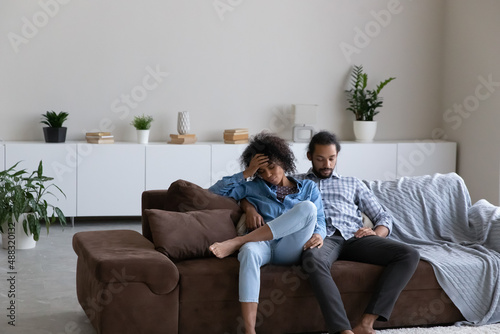 Frustrated young African American couple feeling tired after had working day, resting together on comfortable sofa at home. Unhappy stressed exhausted multiracial man and woman sleeping indoors.