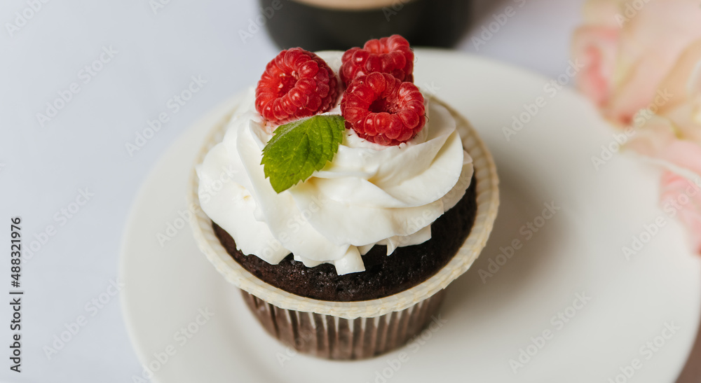 Chocolate muffin with cream and raspberries on a white plate. Chocolate muffin with cream and raspberries on a white plate.