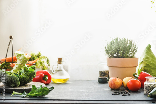 Fototapeta Naklejka Na Ścianę i Meble -  Food background with various vegetables, fruits and potted herbs at kitchen counter at window  background. Healthy cooking at home. Front view.