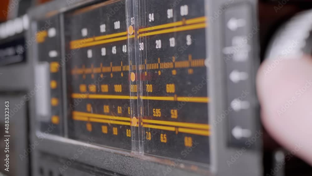 Female Fingers Adjusting the Frequency on an Old Vintage Analog Receiver. Search for a music radio station on a dial scale on panel of a short-wave portable FM radio, player, tape recorder 80s, 90s. Female Fingers Adjusting the Frequency on an Old Vintage Analog Receiver. Search for a music radio station on a dial scale on panel of a short-wave portable FM radio, player, tape recorder 80s, 90s.