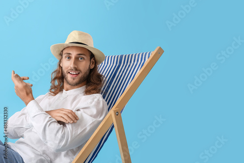 Canvas Print Handsome young man sitting on deck chair against color background