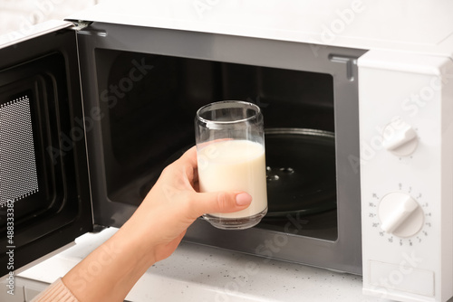 Woman putting glass with milk into microwave oven, closeup