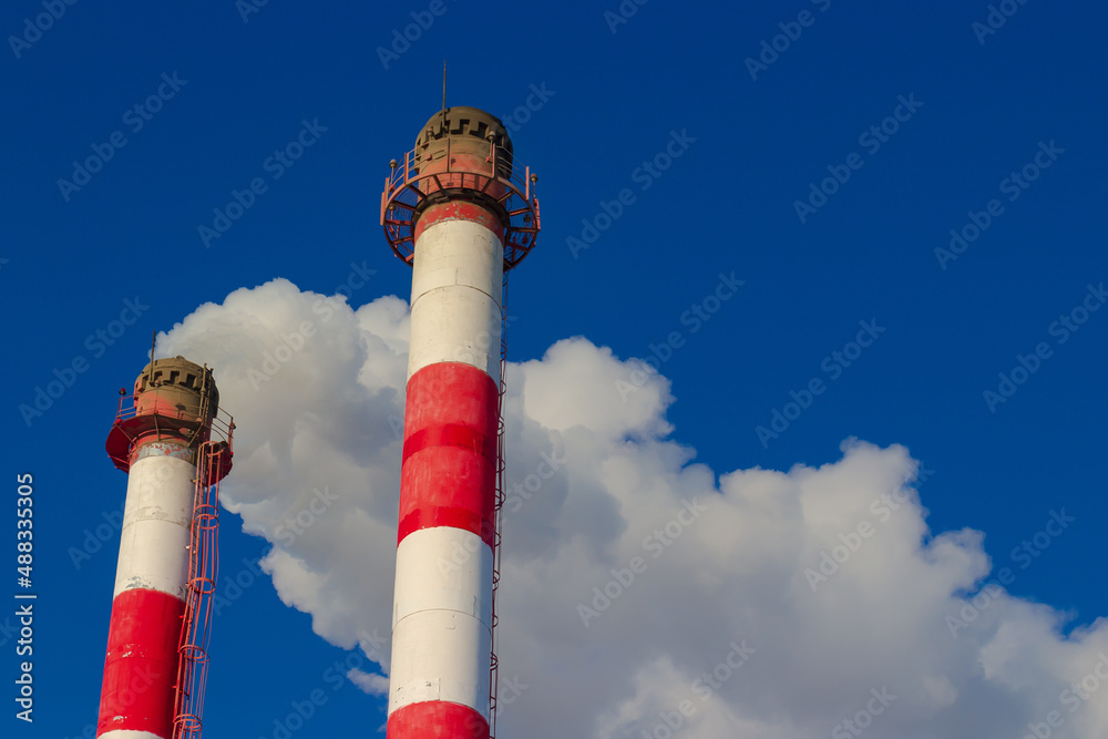 Red and white pipe of boiler plant with white steam and pipe without smoke against blue sky. Heating season in winter. Industrial background. Air pollution from fuel combustion Red and white pipe of boiler plant with white steam and pipe without smoke against blue sky. Heating season in winter. Industrial background. Air pollution from fuel combustion