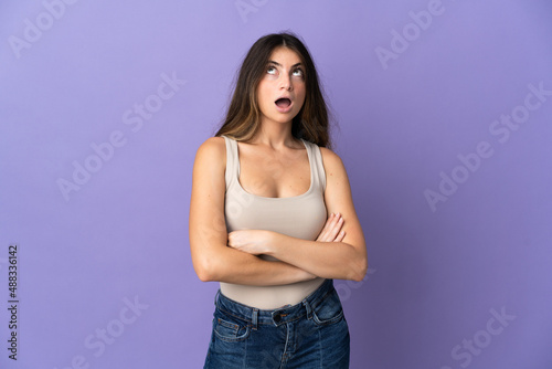 Young caucasian woman isolated on purple background looking up and with surprised expression