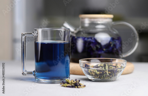 Glass cup of organic blue anchana. Brewed tea in a transparent glass teapot on a gray table. Herbal Thai tea. Selective focus