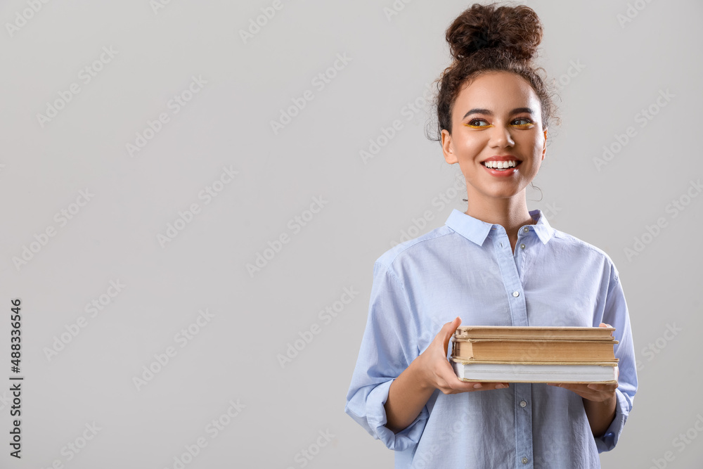 Beautiful young African-American woman with books on grey background Beautiful young African-American woman with books on grey background