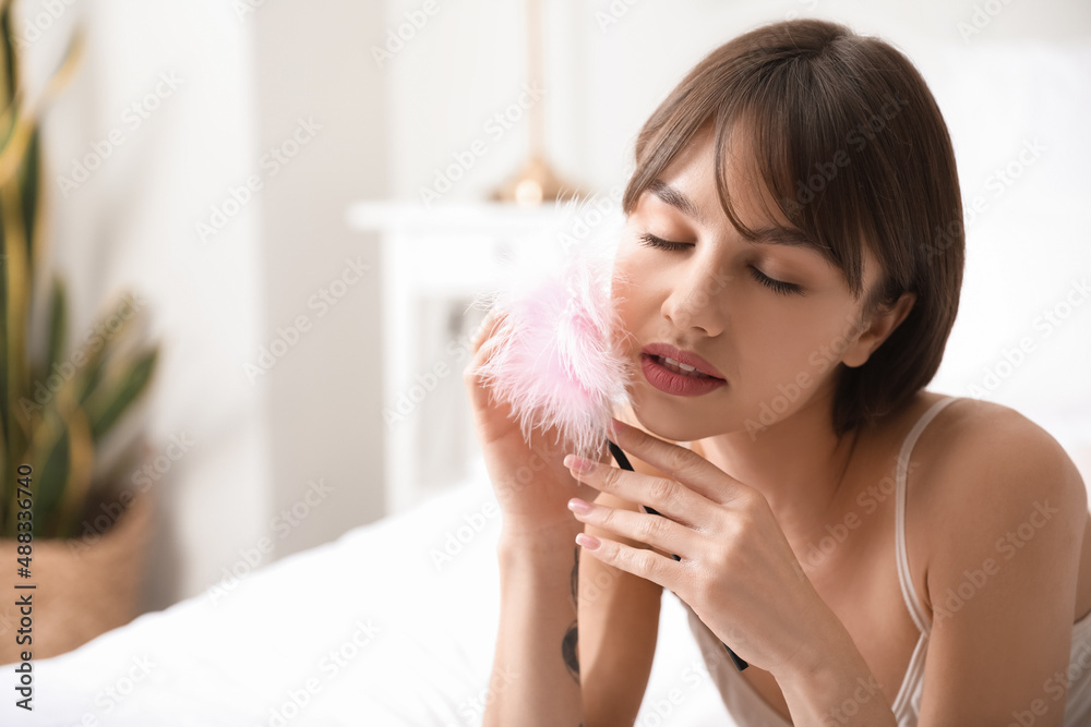Beautiful young woman with feather stick in bedroom