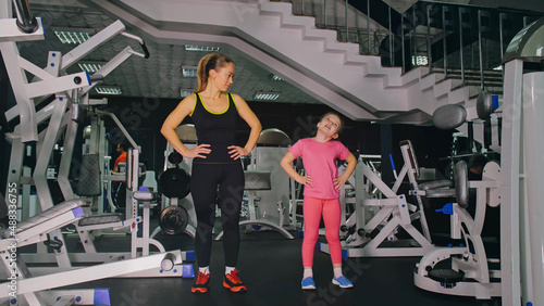 Mother and Daughter in the Gym, Family Performs Physical doing Exercises Fitness, Healthy Lifestyle. Happy Sports Family Training Concept. Woman with her Child doing Stretching Warm-up in the Gym