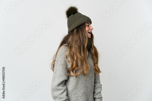 Young caucasian woman with winter hat isolated on white background laughing in lateral position