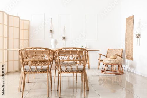 Interior of light dining room with table  wicker chairs and folding screen