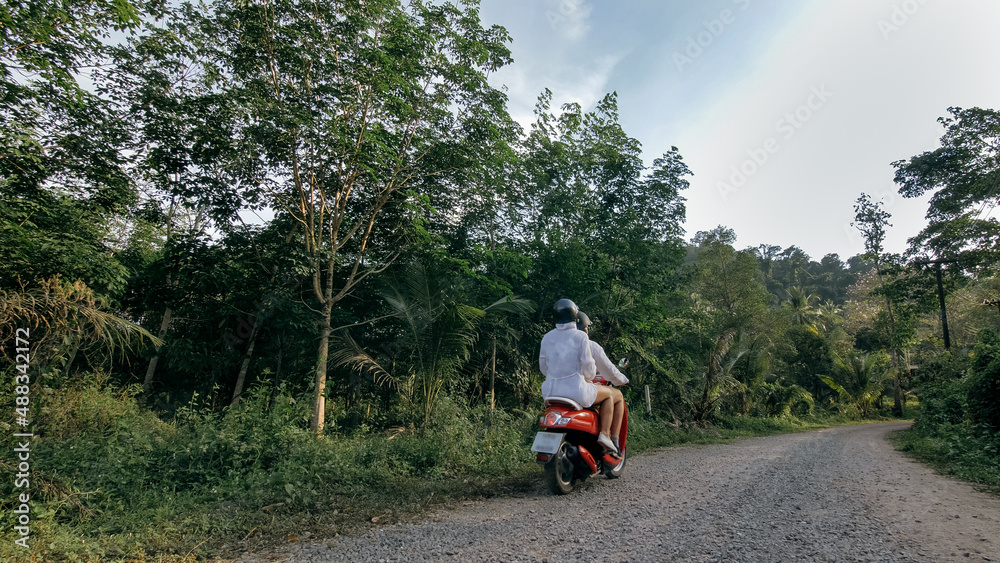 Love couple on red motorbike in white clothes to go on forest road trail trip. Two caucasian tourist woman man drive on scooter. Motorcycle rent, safety helmet, sunglasses. Asia Thailand ride tourism.