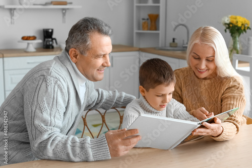 Little boy with his grandparents in warm sweaters reading book at home