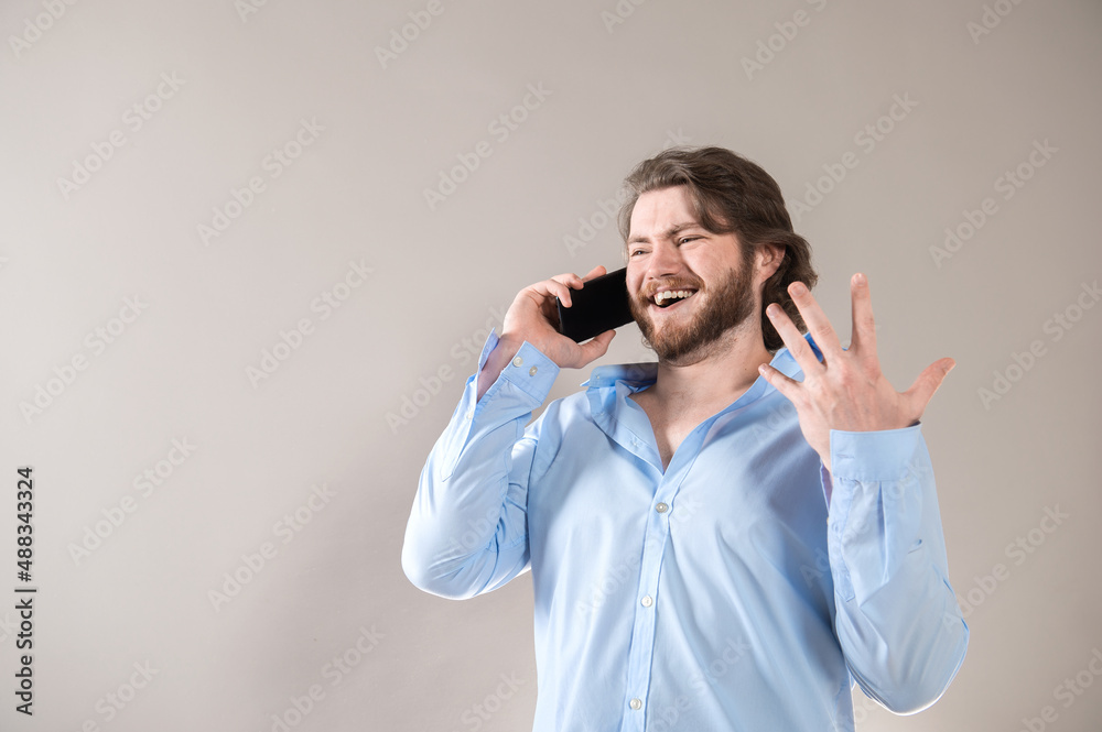 Young bearded man having call and talking on smartphone with pleasure isolated over grey background Young bearded man having call and talking on smartphone with pleasure isolated over grey background