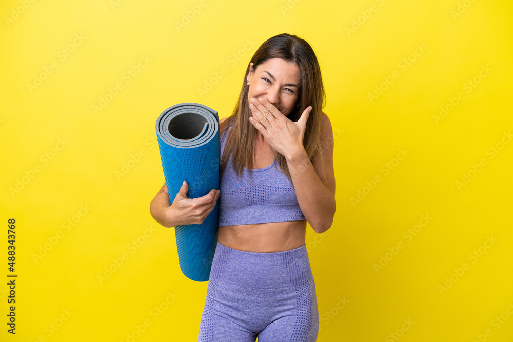 Sport woman going to yoga classes while holding a mat isolated non yellow background happy and smiling covering mouth with hand Sport woman going to yoga classes while holding a mat isolated non yellow background happy and smiling covering mouth with hand