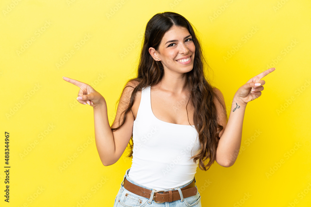 Young caucasian woman isolated on yellow background pointing finger to the laterals and happy Young caucasian woman isolated on yellow background pointing finger to the laterals and happy