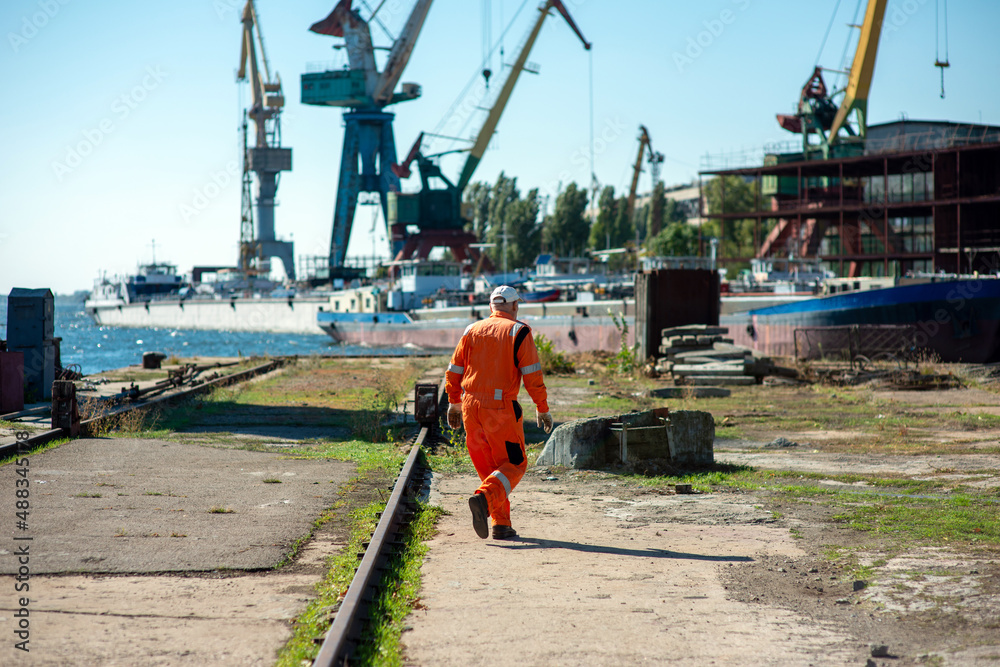 Shipyard worker in overalls against the background of cranes and ships