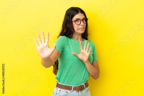 Young caucasian woman isolated on yellow background nervous stretching hands to the front