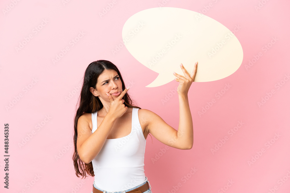 Young caucasian woman isolated on pink background holding an empty speech bubble and thinking Young caucasian woman isolated on pink background holding an empty speech bubble and thinking