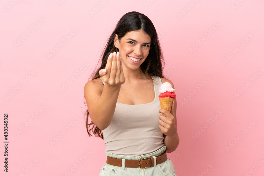 Young caucasian woman with a cornet ice cream isolated on pink background inviting to come with hand. Happy that you came Young caucasian woman with a cornet ice cream isolated on pink background inviting to come with hand. Happy that you came