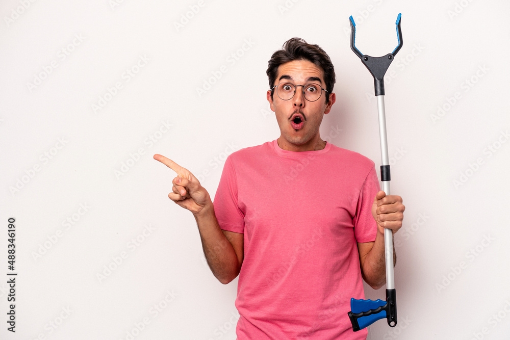 Young caucasian man holding a garbage collector isolated on white background pointing to the side