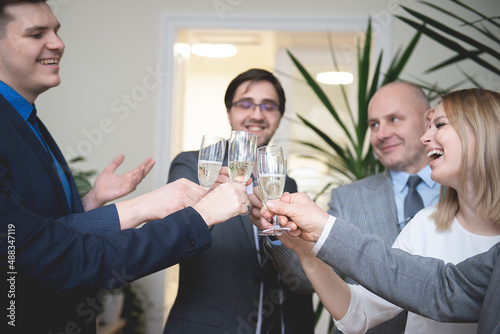 Successful business people are clinking glasses of champagne and smiling while celebrating in office