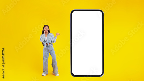 Woman showing white empty smartphone screen and pointing at panel