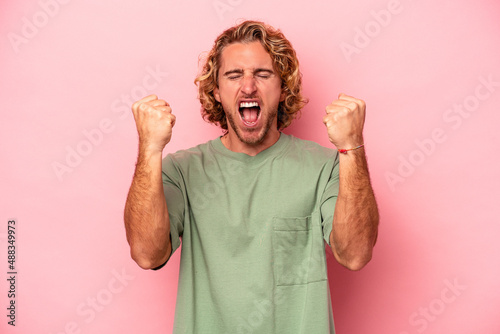 Young caucasian man isolated on pink background cheering carefree and excited. Victory concept.