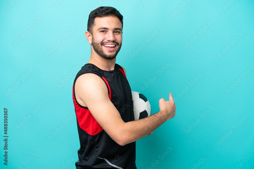Young football player Brazilian man isolated on blue background pointing back