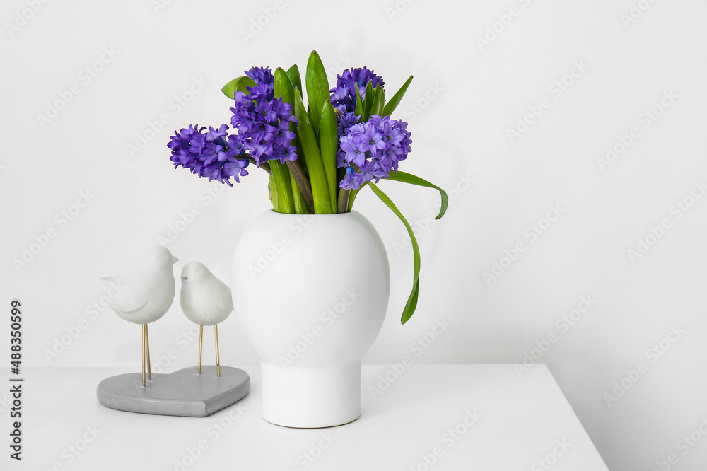 Vase with flowers and decor on table near light wall