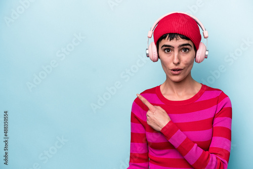 Young caucasian woman listening to music isolated on background pointing to the side
