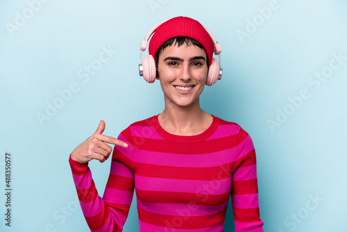 Young caucasian woman listening to music isolated on background person pointing by hand to a shirt copy space, proud and confident
