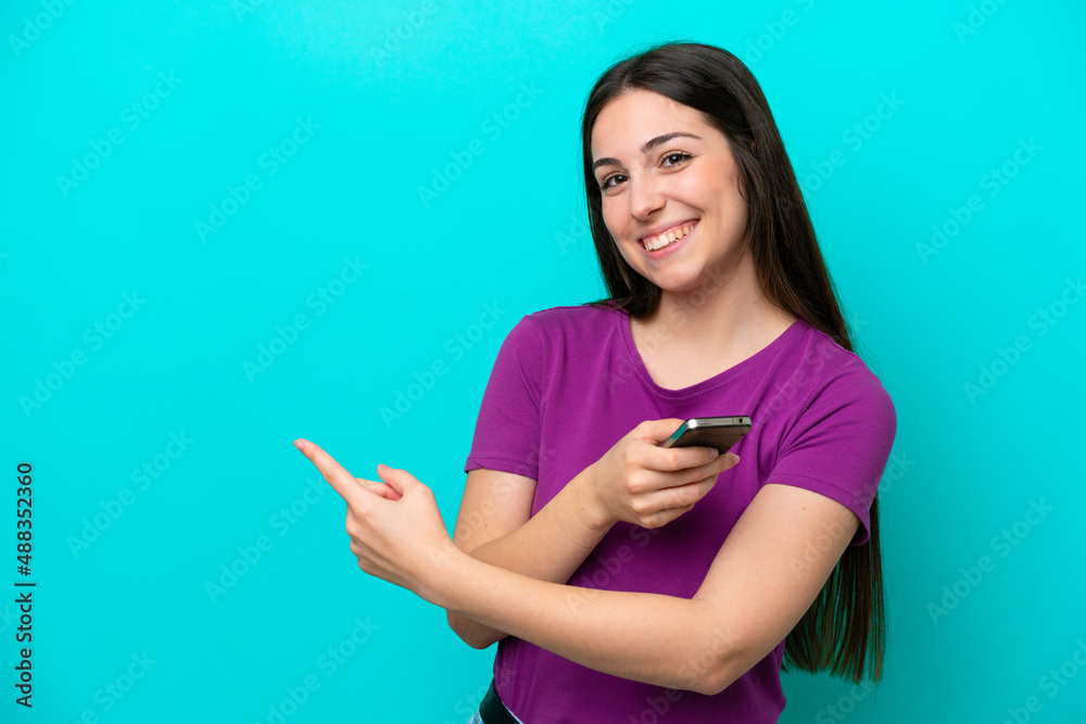 Young girl isolated on blue background using mobile phone and pointing back Young girl isolated on blue background using mobile phone and pointing back