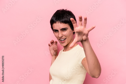 Young caucasian woman isolated on pink background showing claws imitating a cat, aggressive gesture. © Asier