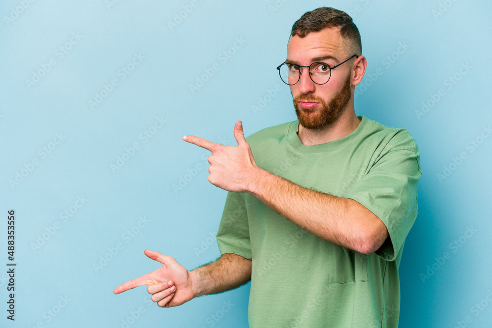 Young caucasian man isolated on blue background shocked pointing with index fingers to a copy space. Young caucasian man isolated on blue background shocked pointing with index fingers to a copy space.