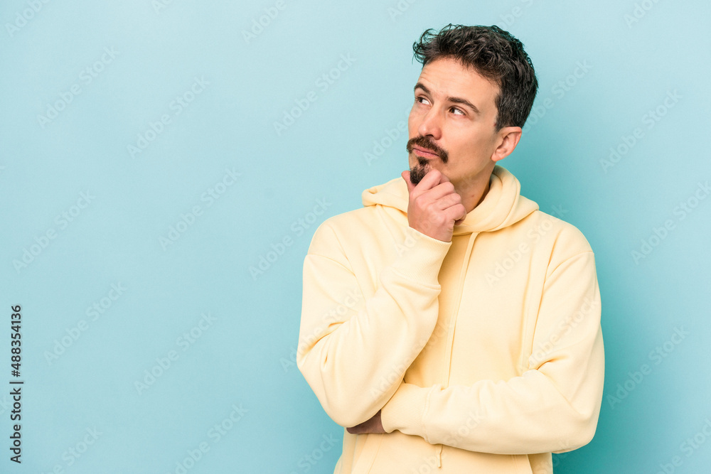 Young caucasian man isolated on blue background looking sideways with doubtful and skeptical expression.