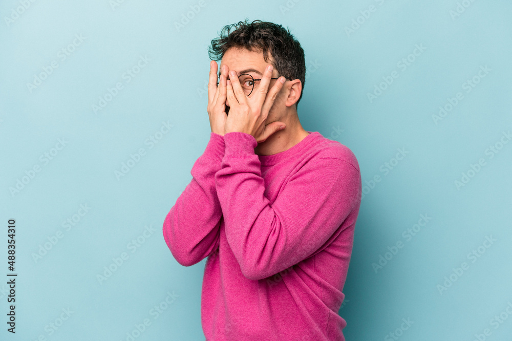 Young caucasian man isolated on blue background blink through fingers frightened and nervous. Young caucasian man isolated on blue background blink through fingers frightened and nervous.