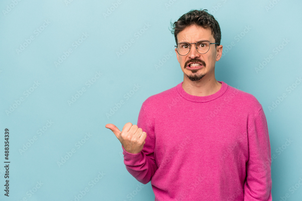 Fototapeta premium Young caucasian man isolated on blue background shocked pointing with index fingers to a copy space.