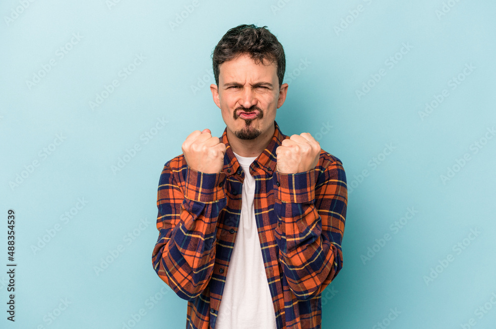 Young caucasian man isolated on blue background showing fist to camera, aggressive facial expression.